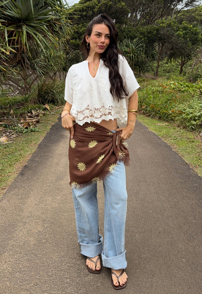 Front view of Melo Brown Modal scarf tied at waist over jeans, showing golden sun print and frayed edge detail