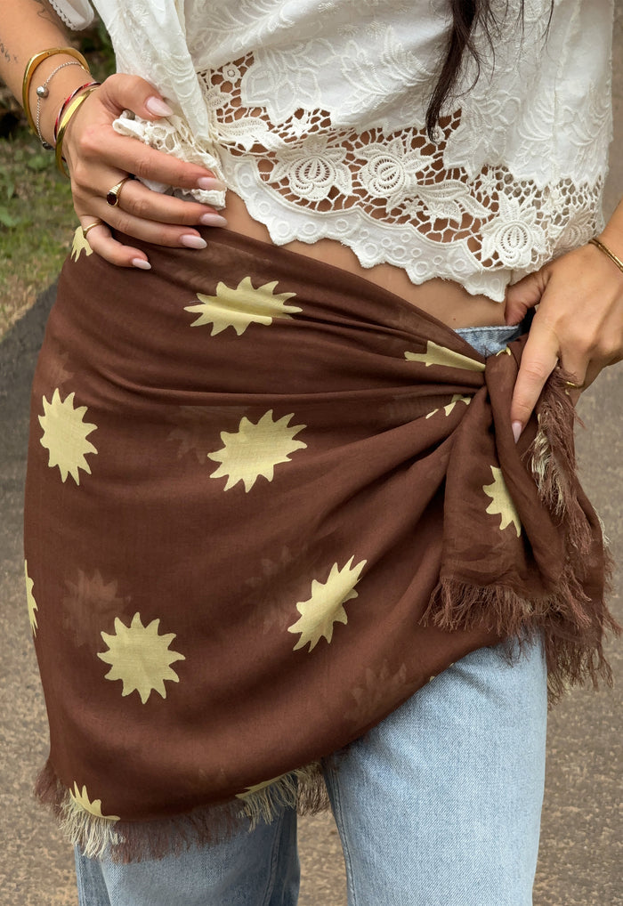 Brown Modal scarf with gold sun print tied as wrap skirt over jeans, showing frayed edge detail