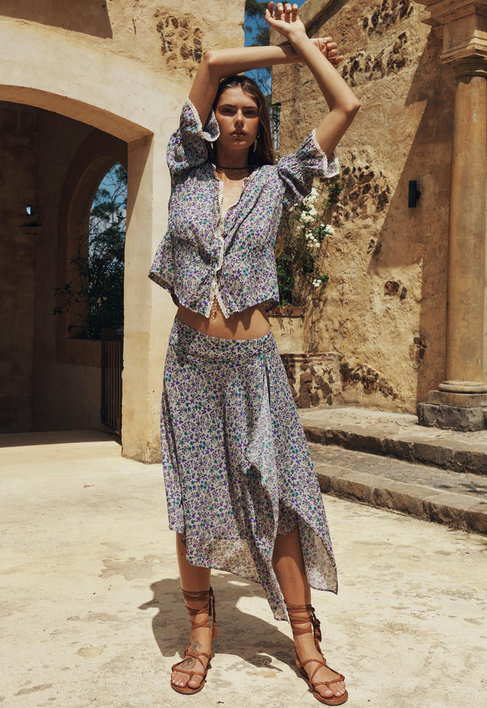 Model wearing Violet Fields floral midi skirt front view, asymmetric waterfall hem, with matching tie-front top
