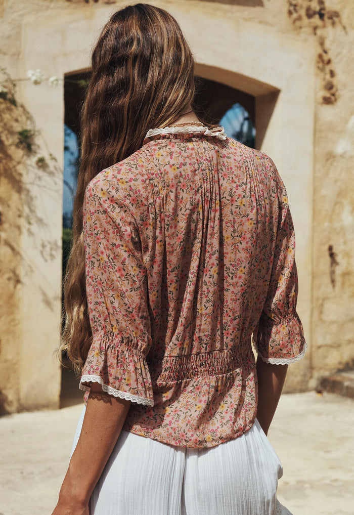 Back view of a model wearing Pink Posey blouse, showing pintuck back, shirred waist, and lace-trim sleeve hem