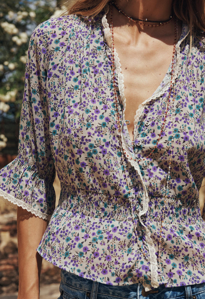 Close-up front view of violet floral blouse showing lace-trim V-neckline, button front, and shirred waist detail