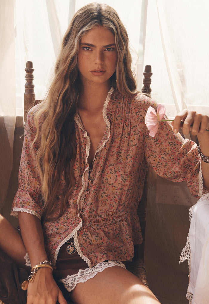 Model seated front-facing in Pink Posey floral blouse, lace-trim neckline and shirred waist visible