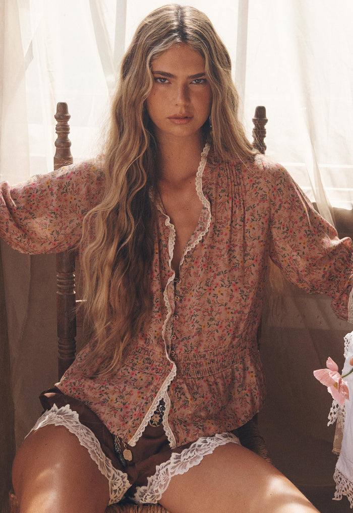 Model seated front-facing, lace-trim neckline and shirred waist detail visible on Pink Posey blouse