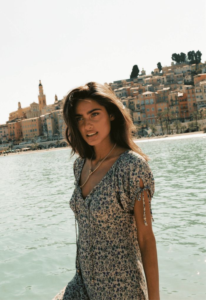 Model wearing Mimi-Rose Mini Dress, front view, gathered neck and tie sleeves visible, coastal backdrop