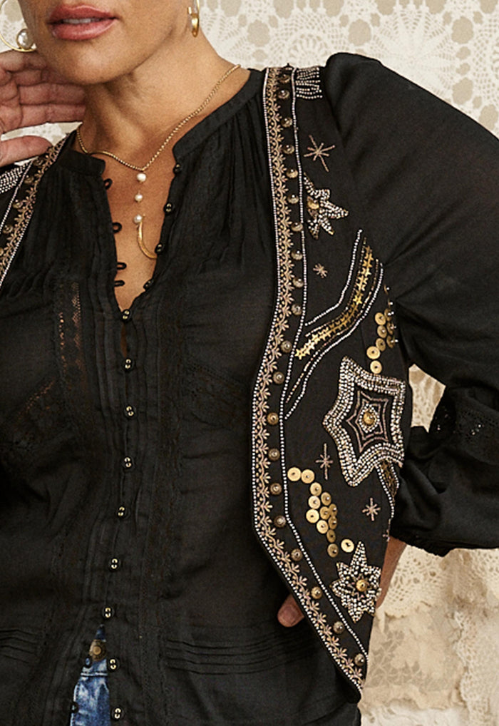 Close-up of gold sequin and bead embellished trim on black vest front, showing button placket and lace panel detail