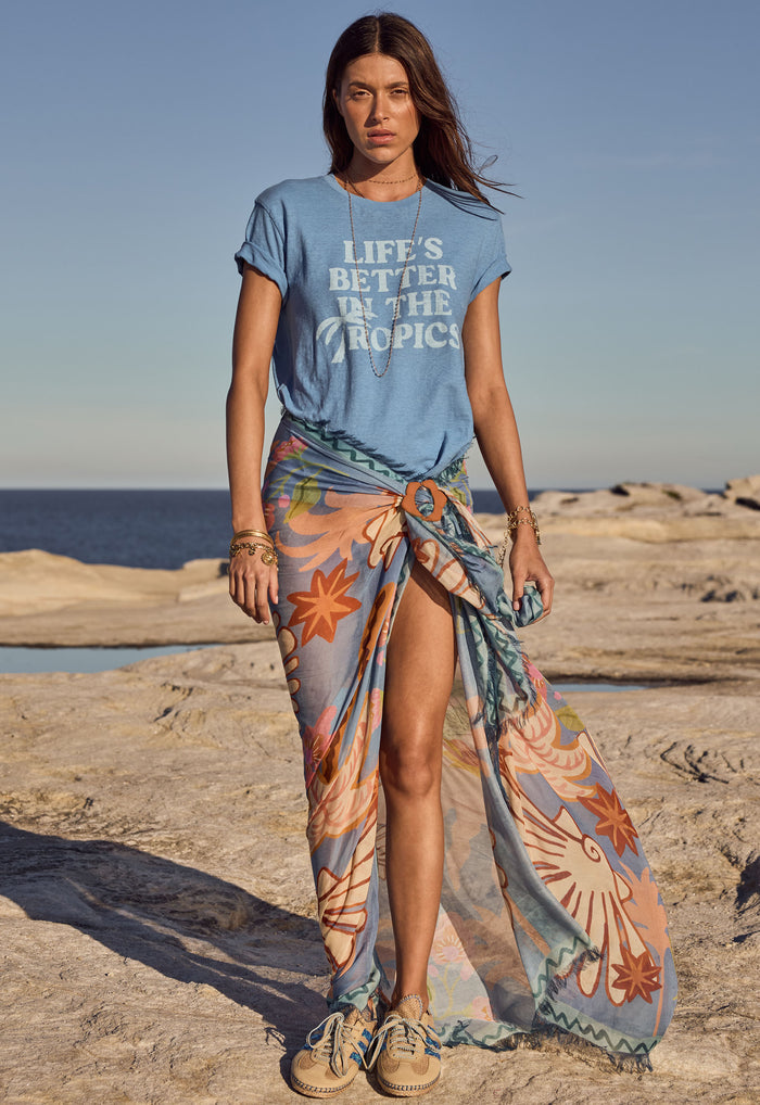 Oceana Travel Scarf in Sea Blue Modal worn as sarong with buckle, front view on coastal rocks