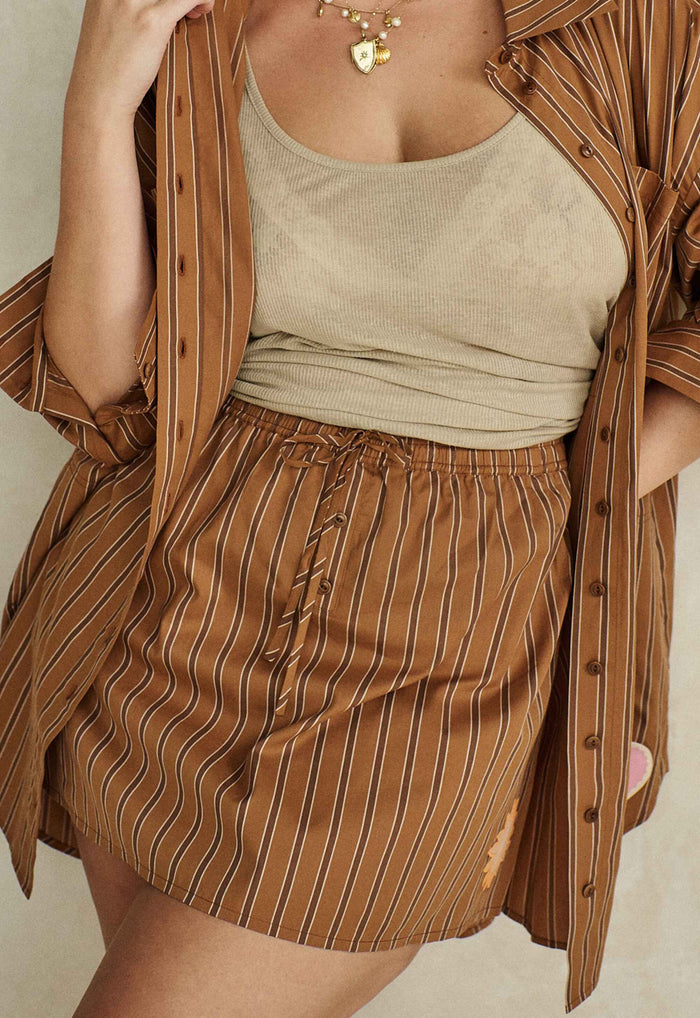 Front view of striped organic cotton mini skirt with button placket, elastic waist tie, styled open over a ribbed tank