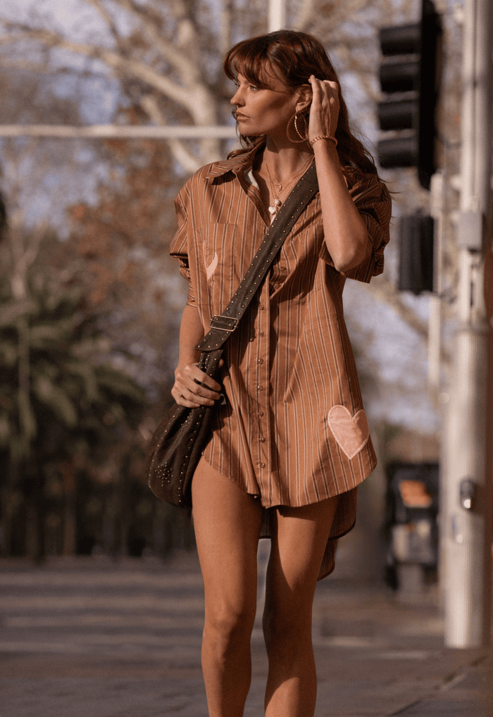 Model in caramel stripe organic cotton oversized shirt, side view showing heart applique detail on hem