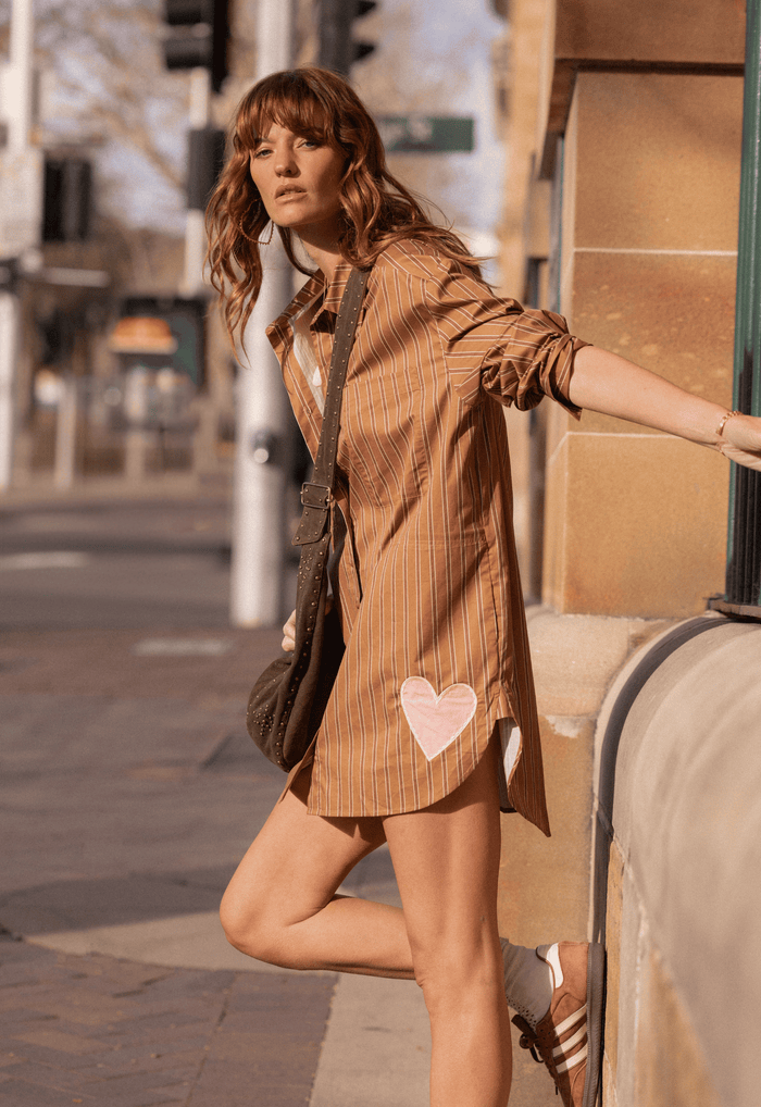 Model wearing caramel stripe organic cotton shirt dress, heart applique hem detail, styled with crossbody bag