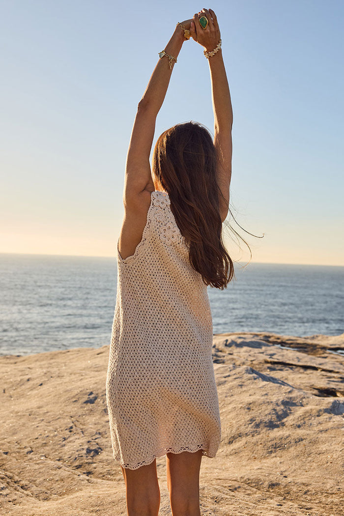 Back view of cream crochet mini dress showing scallop knit hem and open back on rocky coastal setting