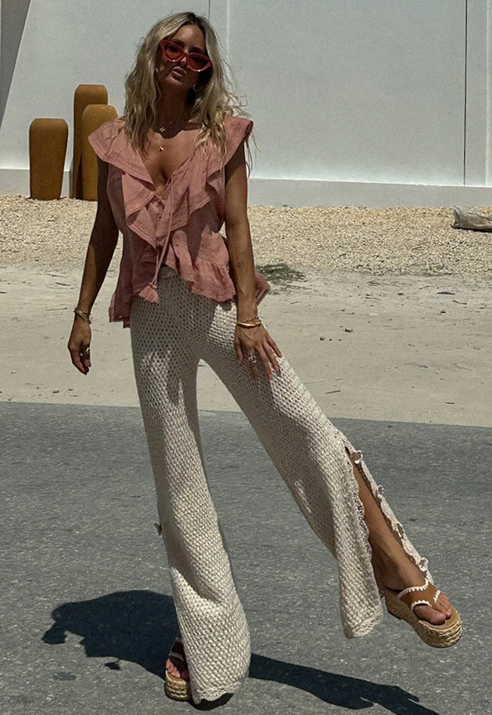 Front view of cream knit flare pants with scallop hem edge and side slits, styled with a pink ruffle top outdoors