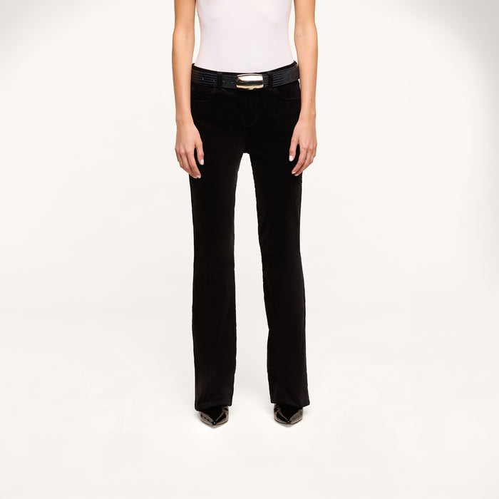 A person wearing a white sleeveless top, the Petite Stevie Velvet Jean with a belt, and black pointed shoes stands against a plain white background, facing forward.