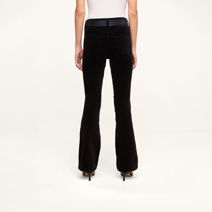 A person is seen from the back, standing against a plain white background, wearing the Petite Stevie Velvet Jean styled with heeled shoes.