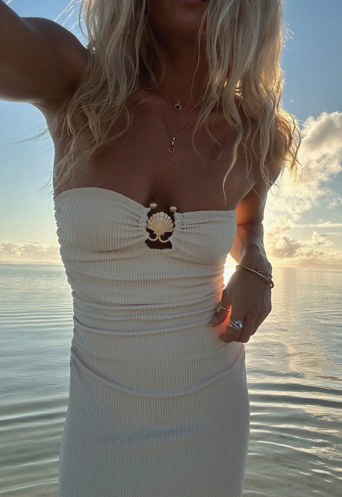 Close-up of cream ruched strapless bodice with custom gold shell hardware detail, ocean backdrop at sunset