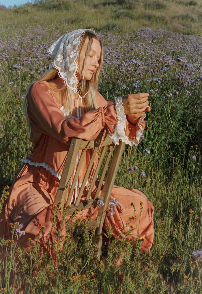 Model kneeling in wildflower field, lace-trim cuffs and hem detail visible on rose TENCEL blouse