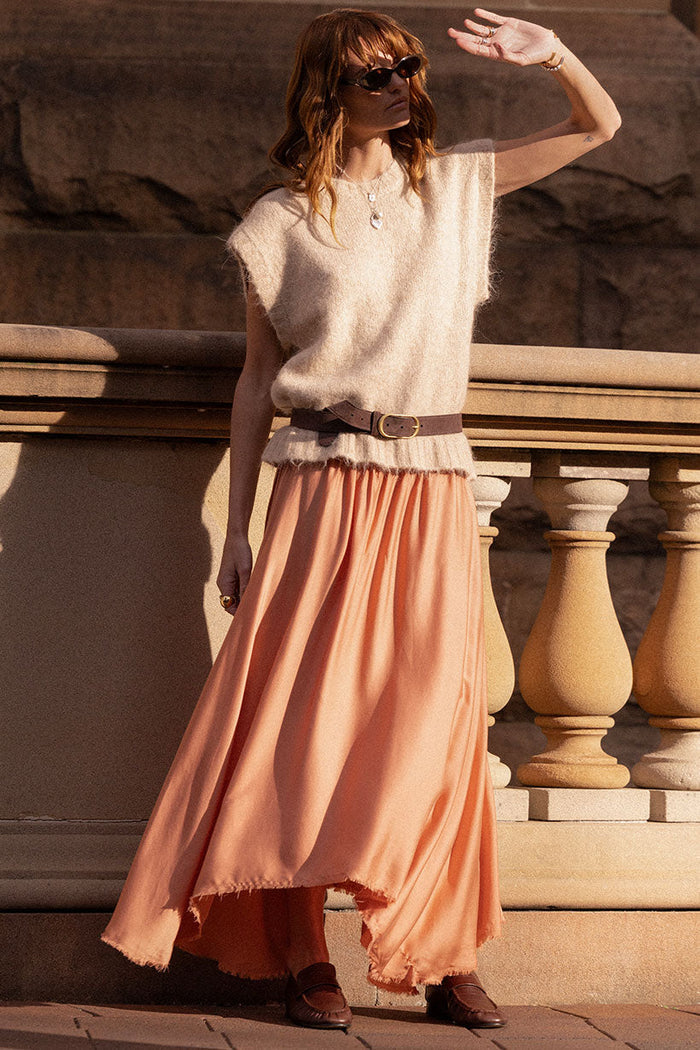 Model wearing rose TENCEL maxi skirt with frayed hi-lo hem, belted with knit top, stone balustrade backdrop