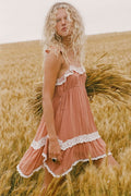 Side view of a model in rose Poison Peach Mini Dress, lace-trim hem and frill neckline, wheat field setting