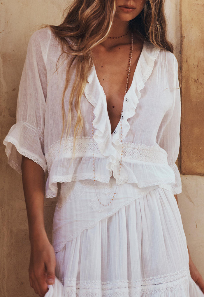 Model wearing Prairie Blouse front view, deep V-neck with ruffle lace trim and embroidered waist detail in whisper white