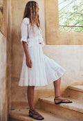 Model side profile wearing white organic cotton Prairie Midi Skirt, tiered gathered hem, lace trim, stone steps