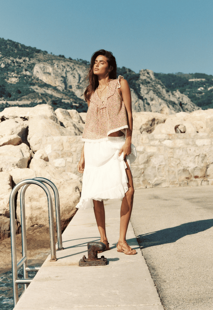 Model wearing Prairie Midi Skirt side view, showing gathered hem frill and organic cotton drape, coastal setting