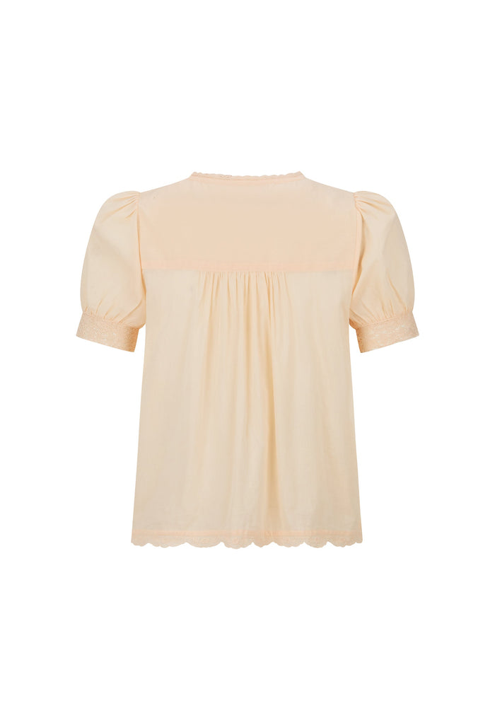 A light peach-colored blouse with short puff sleeves, a gathered smocked bodice, and a scalloped hem, shown against a plain white background.