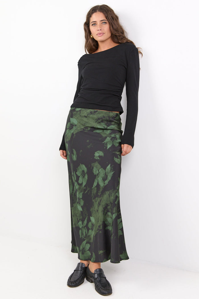Woman wearing a black top and green patterned skirt on a white background