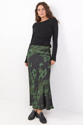 Woman wearing a black top and green patterned skirt on a white background