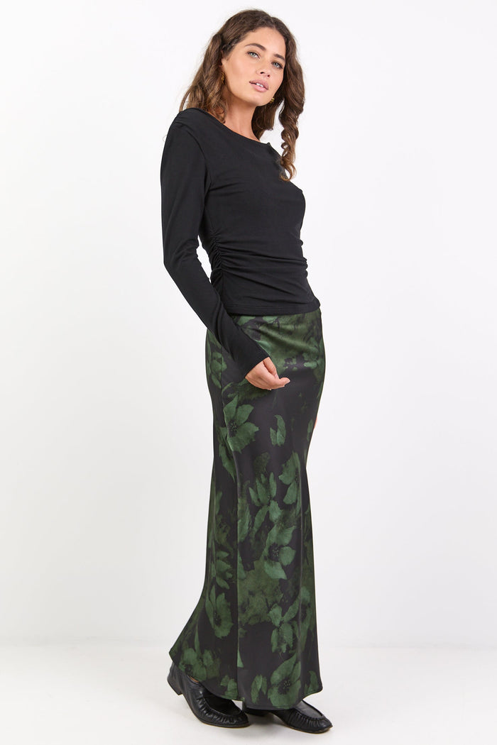 Woman wearing a black long-sleeve top and green patterned skirt on a white background