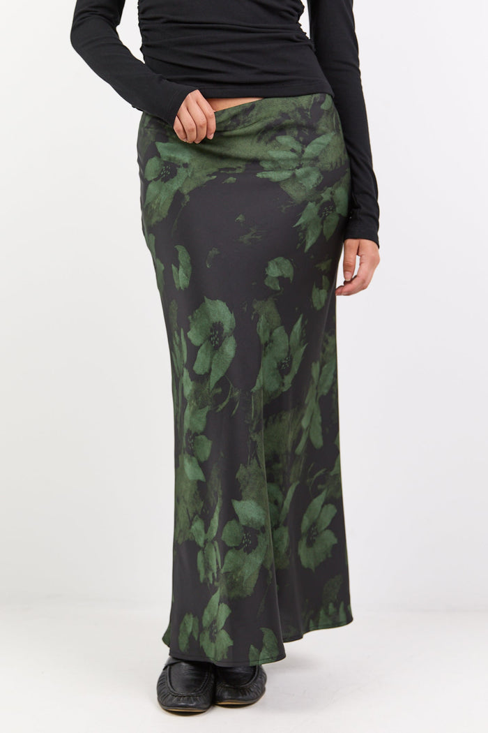 Person wearing a black long-sleeve top and green patterned skirt on a white background