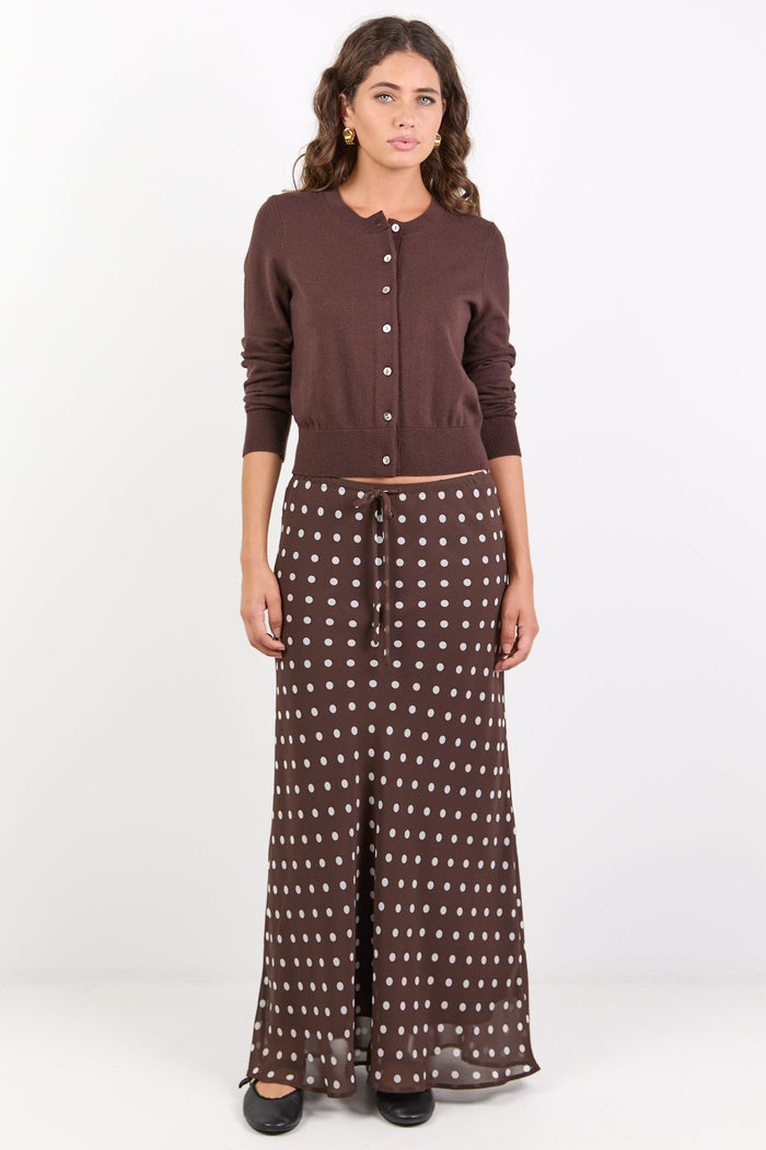 Woman wearing a brown cardigan and patterned skirt on a white background