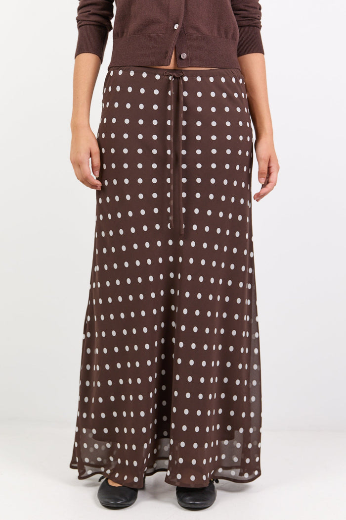 Woman wearing a brown cardigan and patterned skirt on a white background