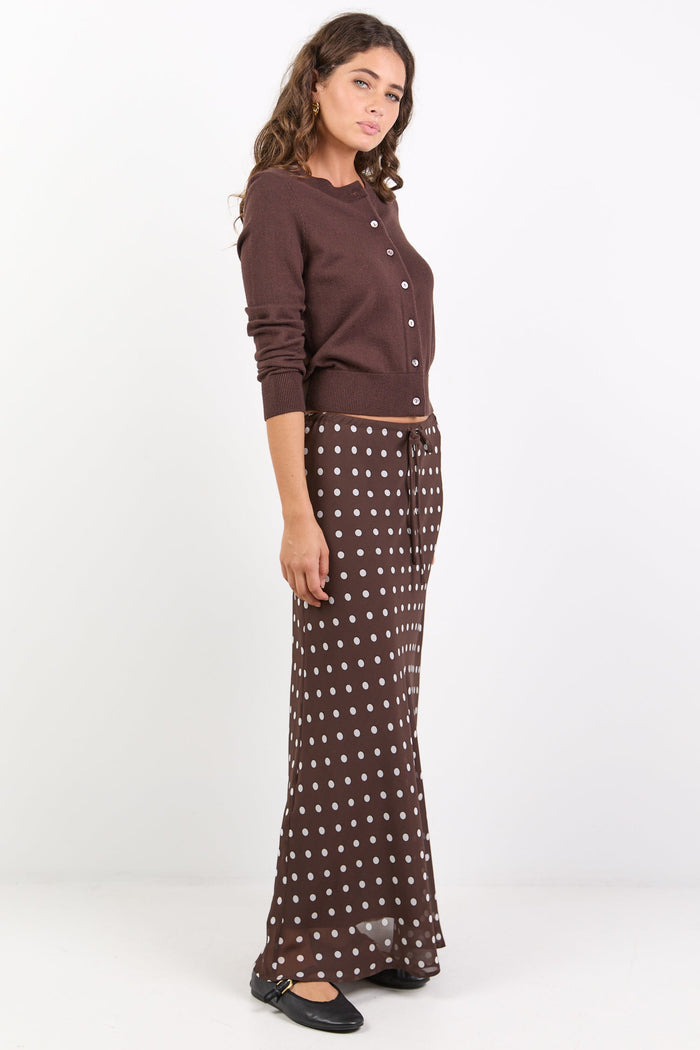 Woman wearing a brown long-sleeve top and patterned skirt on a white background