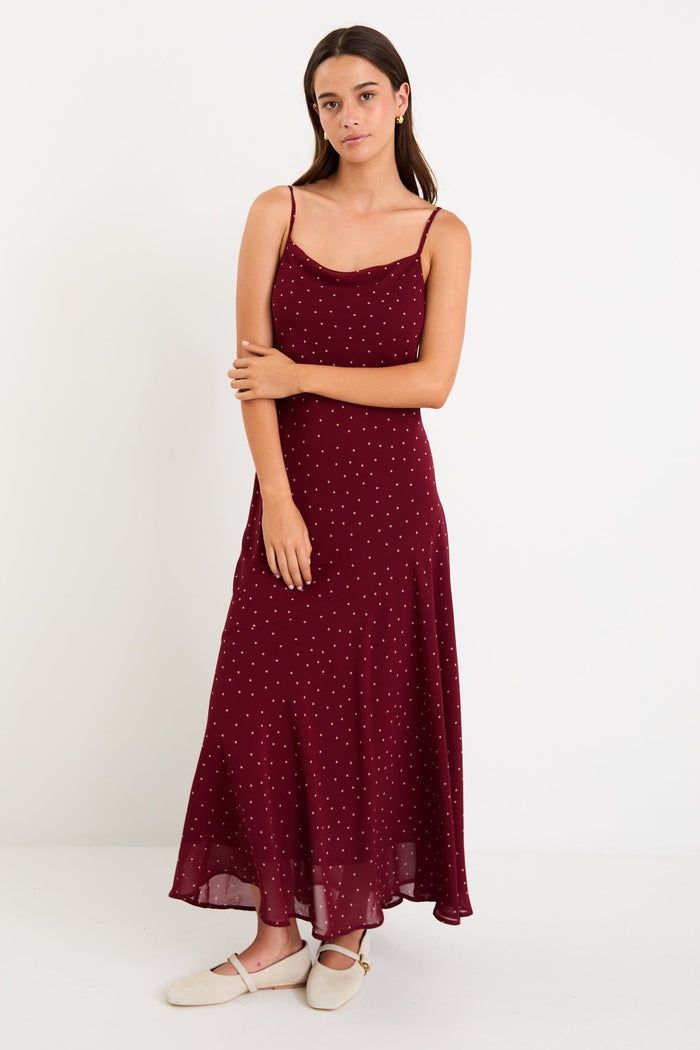 Model wearing a burgundy polka dot strappy maxi dress with a bias-cut silhouette and a flowy skirt