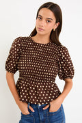 Model wearing a chocolate brown polka dot short sleeve top with a shirred bodice and peplum hem
