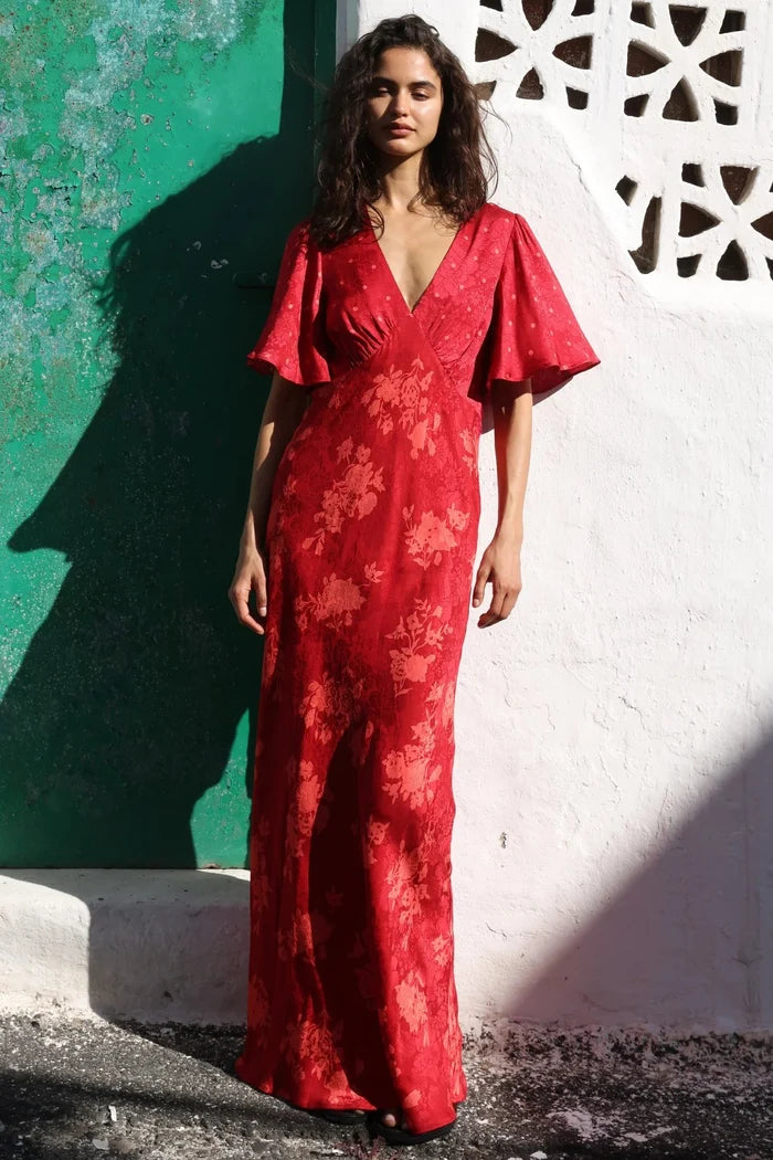 Woman in a red floral dress standing against a white wall with geometric design.