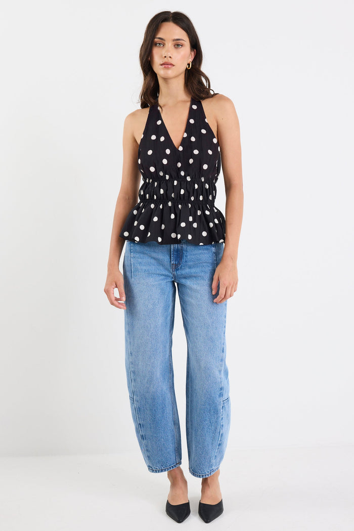 Woman wearing a black sleeveless top with white patterns and blue jeans on a white background