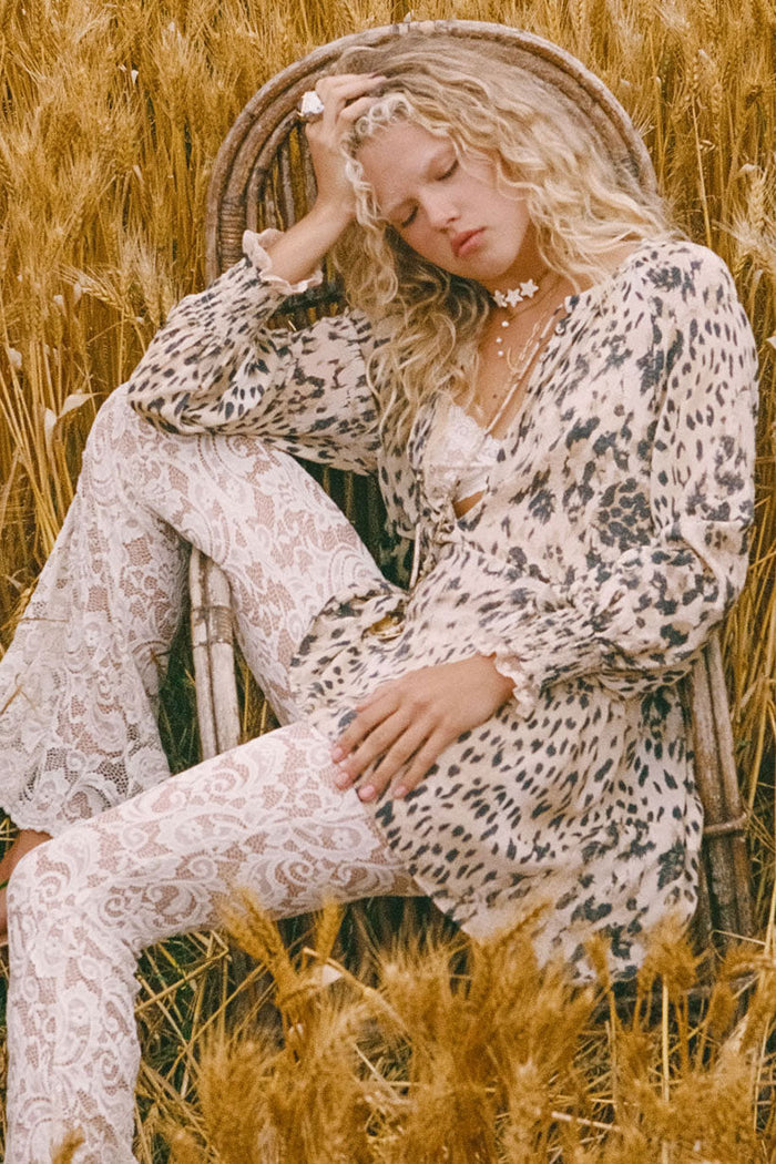 Model seated in wheat field, front view showing snow leopard print, lace trim, front neck ties and shirred cuffs