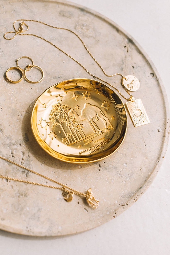 An overhead image of gold jewellery surrounding the gold plated Spell Jewellery Dish with a ‘starry night with camels’ etching.