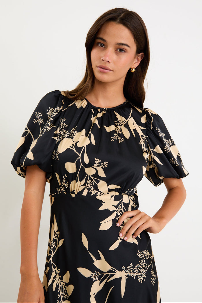 Woman wearing a black dress with gold floral patterns on a white background