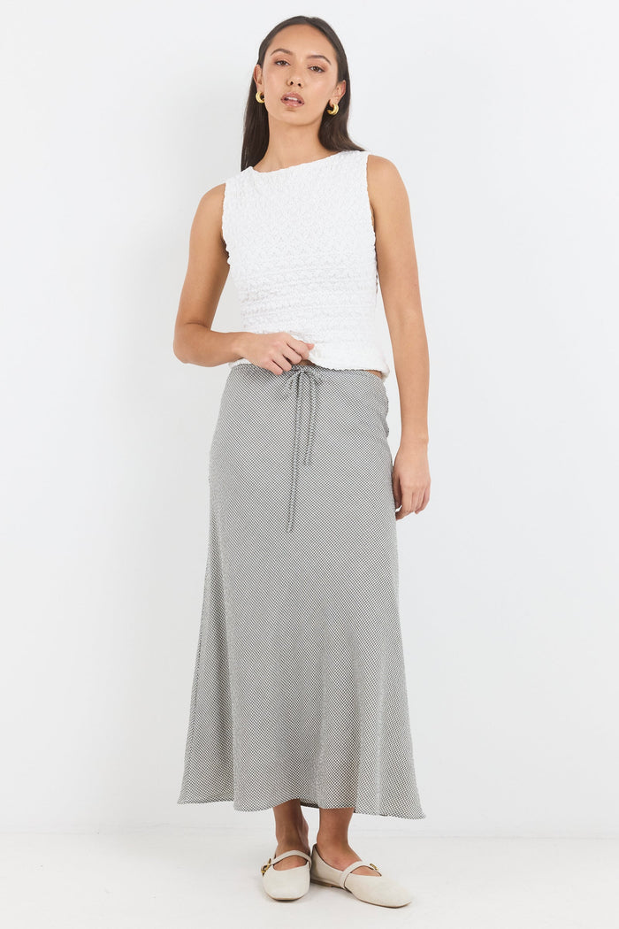 Woman wearing a white sleeveless top and gray skirt on a white background