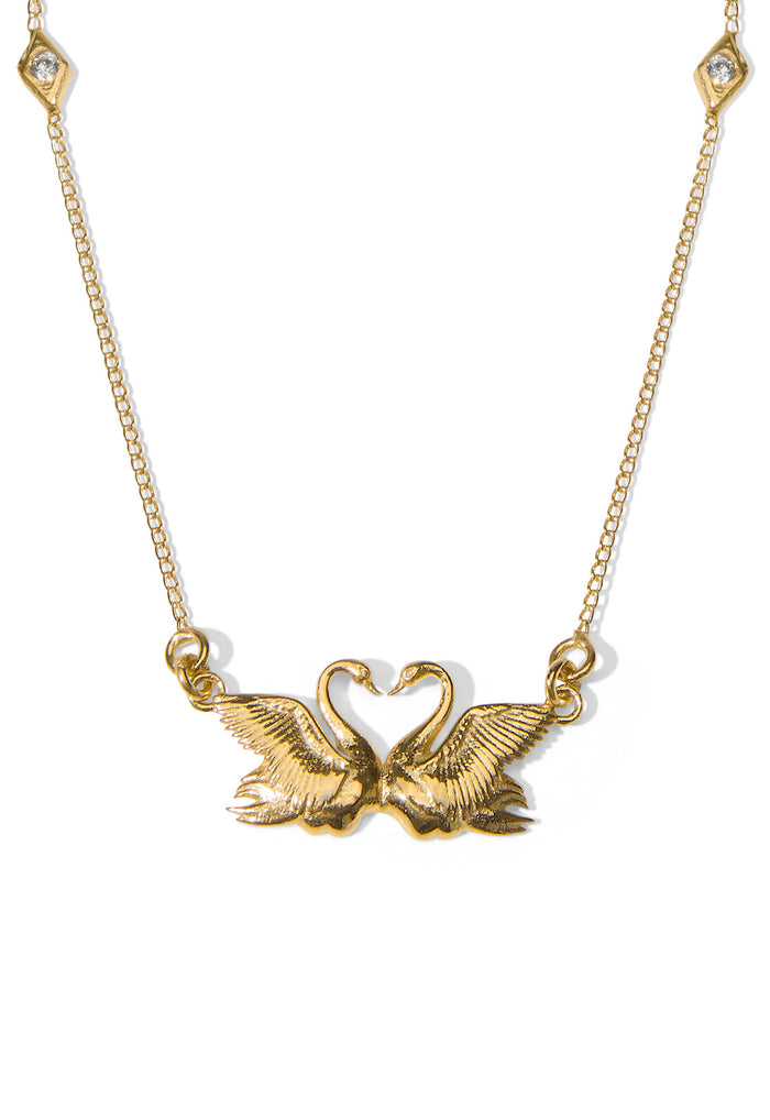 Swan Lake Necklace flat lay, dual swan pendant forming heart, diamond crystal chain stations, 22k gold-plated brass