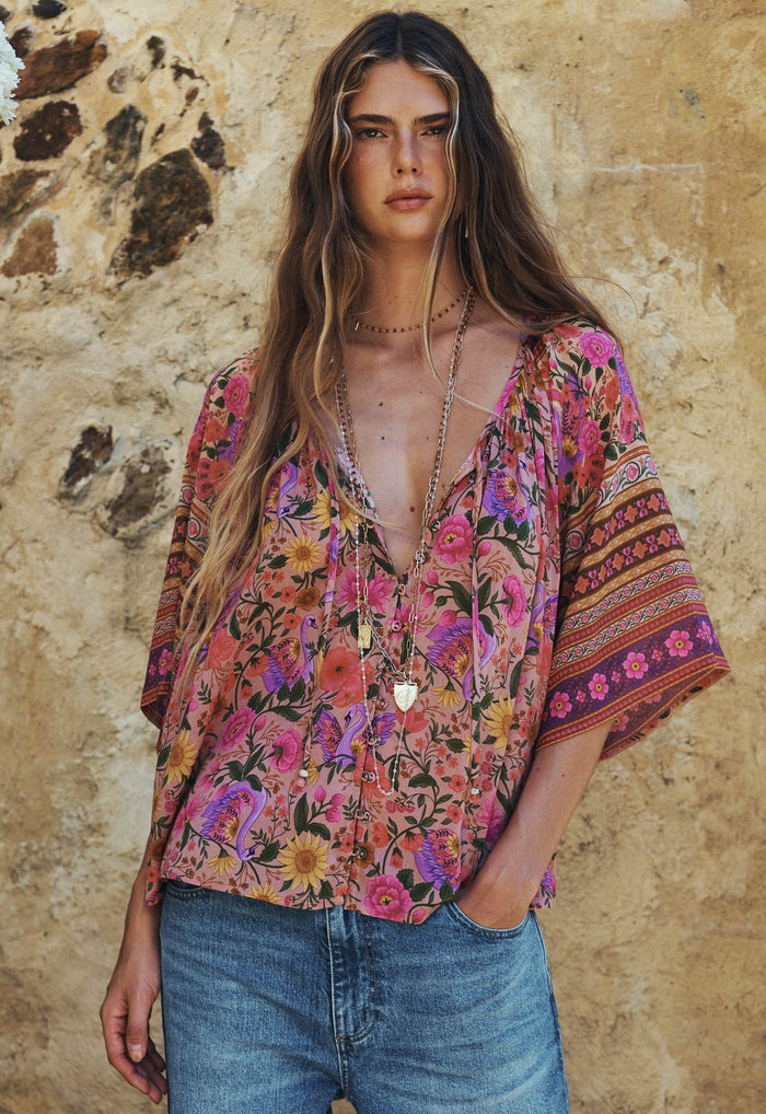 Model wearing Swan Lake blouse front view, floral allover print, V-neck with beaded neck tie, hip-length fit