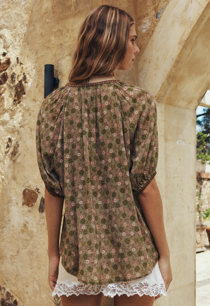 Back view of a model wearing Swan Lake blouse, sage floral ECOVERO viscose with elastic sleeve hems and contrast border trim