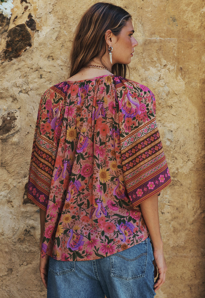 Back view of a model wearing Swan Lake blouse, gathered neck and wide sleeves with border print in lilac rose floral