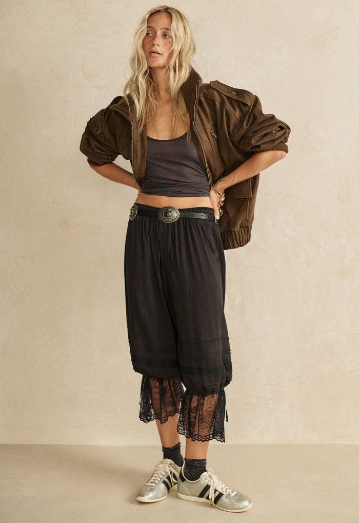Model wearing black lace-hem pantaloons front view, elastic waist with pintucks, self ties at ankles, styled with belt
