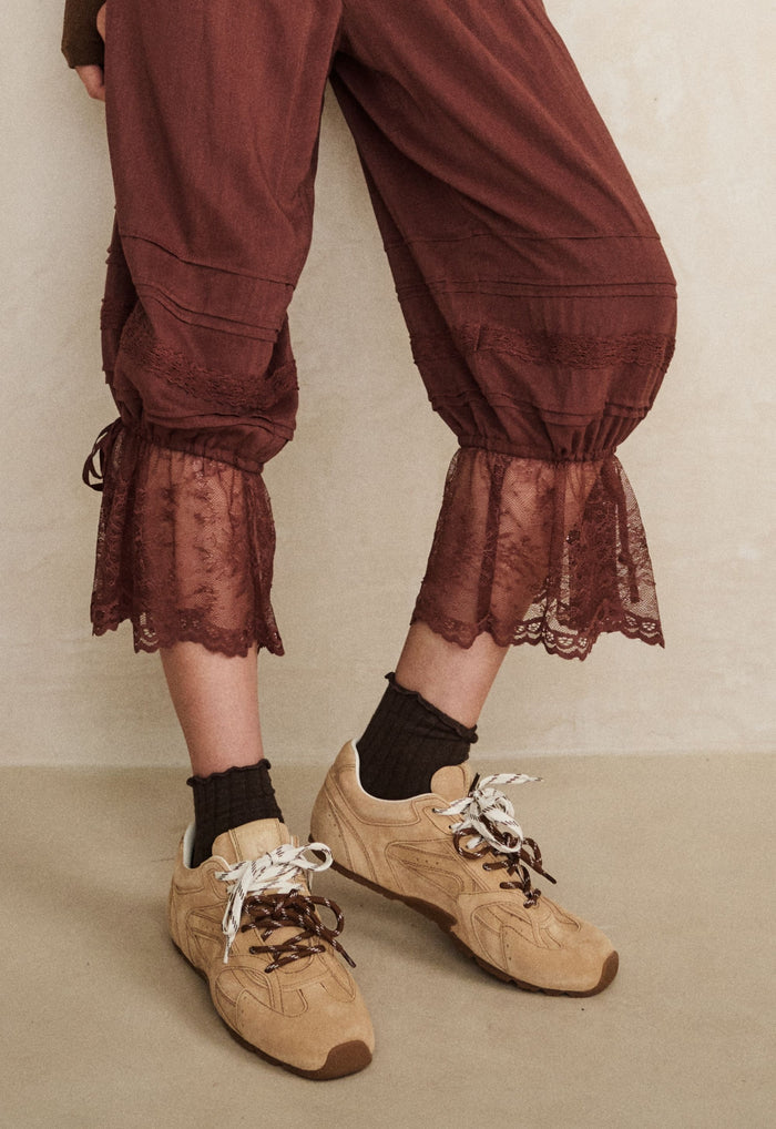 Close-up of lace hem cuffs on fudge pantaloons with self-tie ties, styled with tan sneakers and dark socks