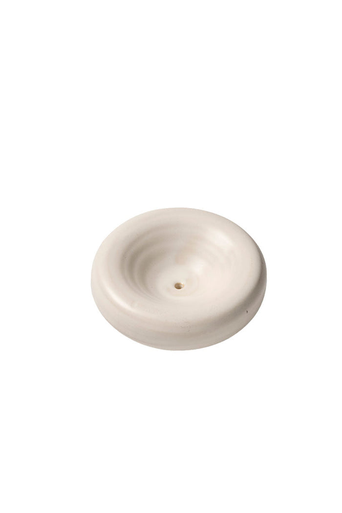 Top-down angle of round cream ceramic incense holder with central stick opening and ridged surface