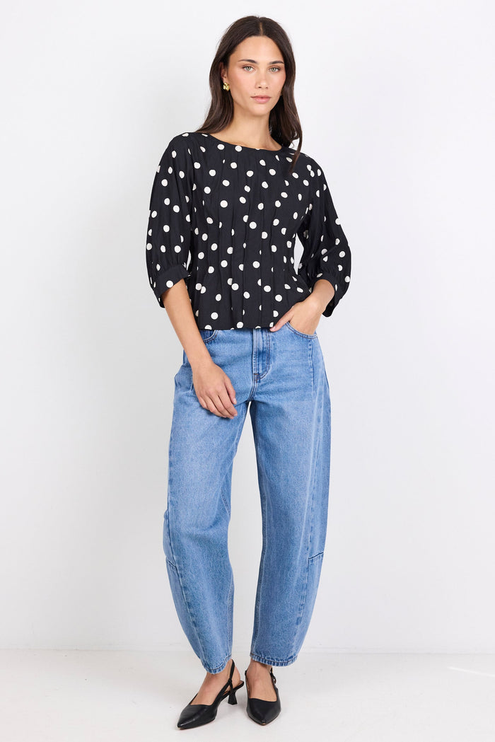 Woman wearing a black polka dot blouse and blue jeans on a white background