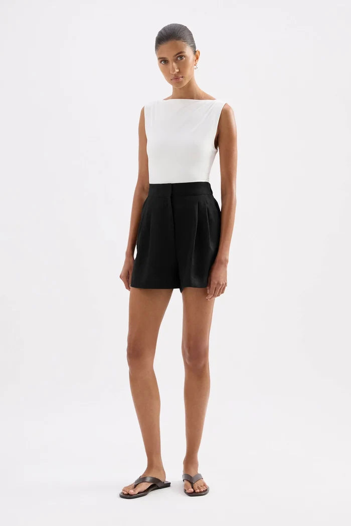 A model wearing a sleeveless white top and black shorts, standing against a plain white studio background.