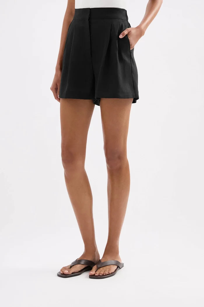 A model wearing black high-waisted shorts with side pockets and brown leather slide sandals, shown from the waist down against a plain white studio background.